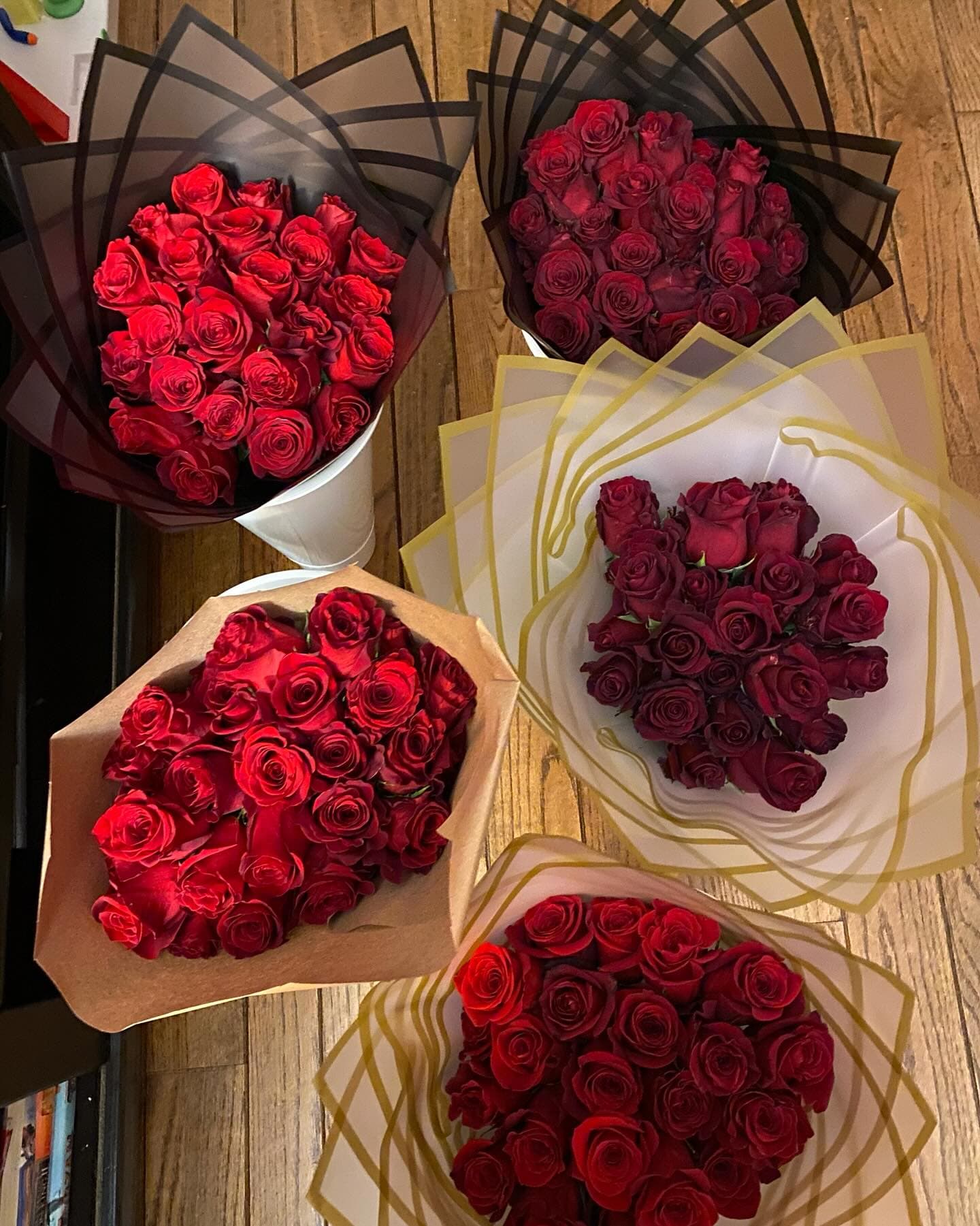 Five bouquets of red roses wrapped in black, brown, and white paper on wooden floor.