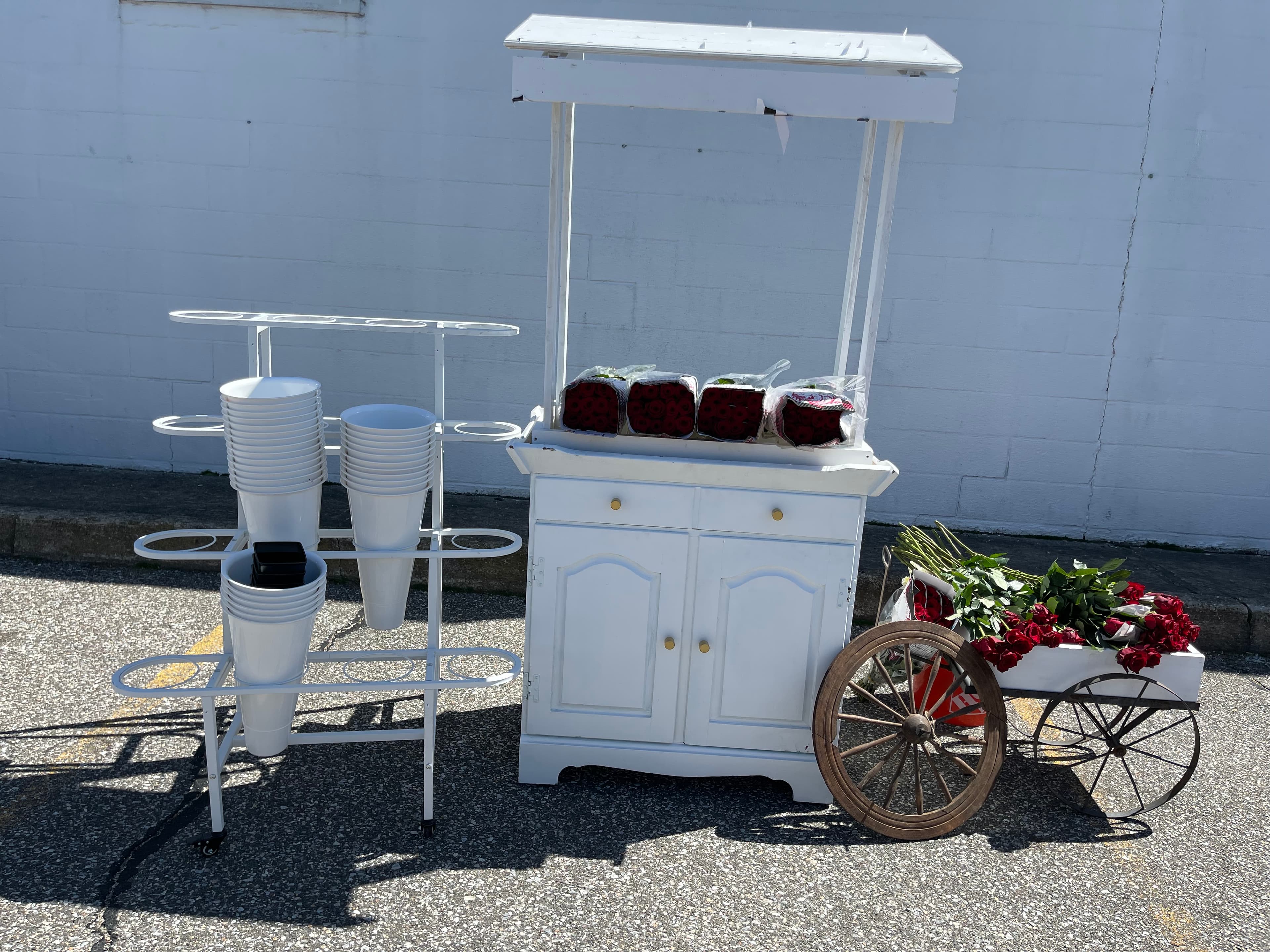 White wooden flower cart with red roses, a bucket rack, and a small wooden wagon.