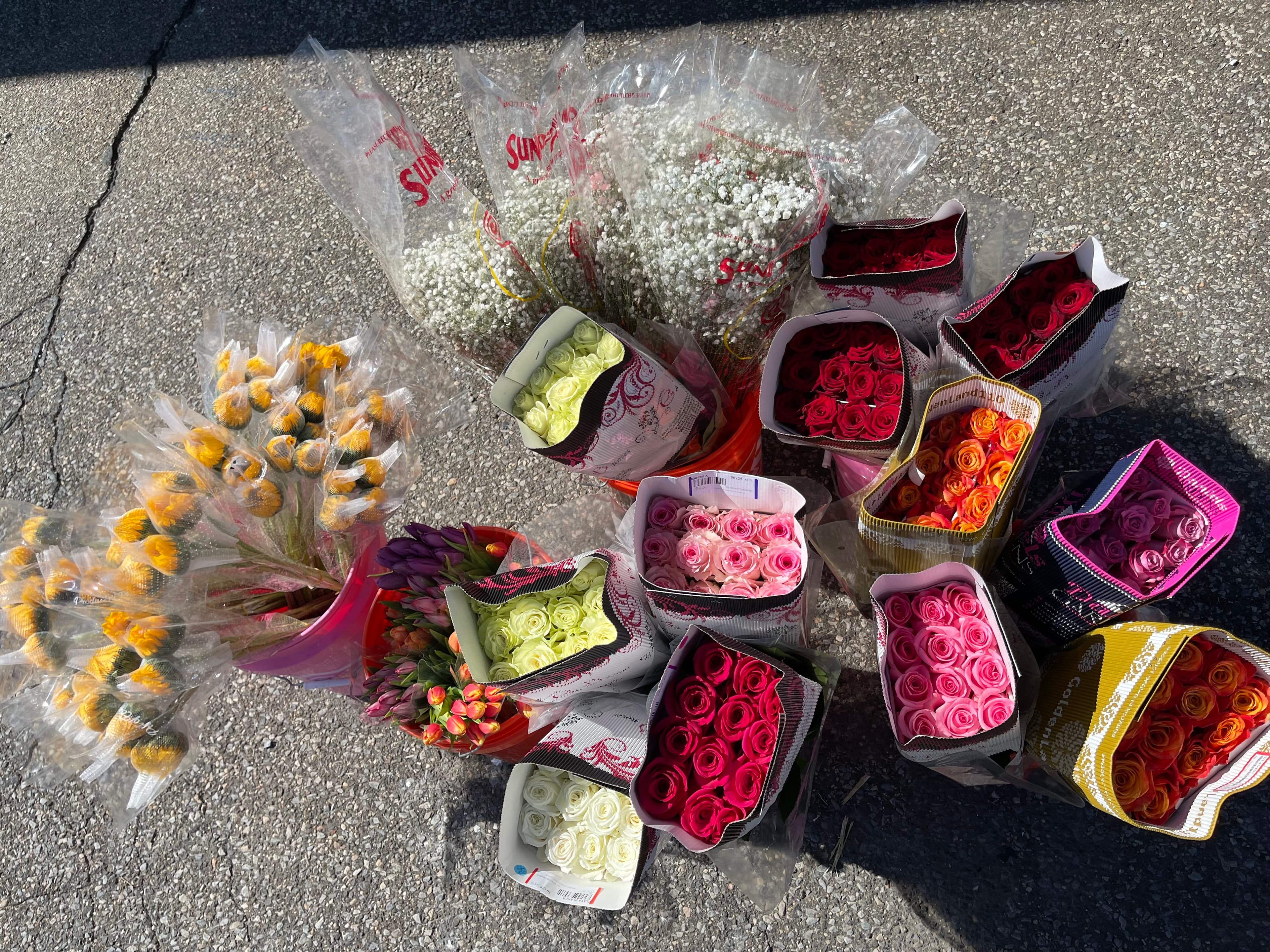 Assorted colorful bouquets of roses and baby's breath arranged on a grey asphalt surface.