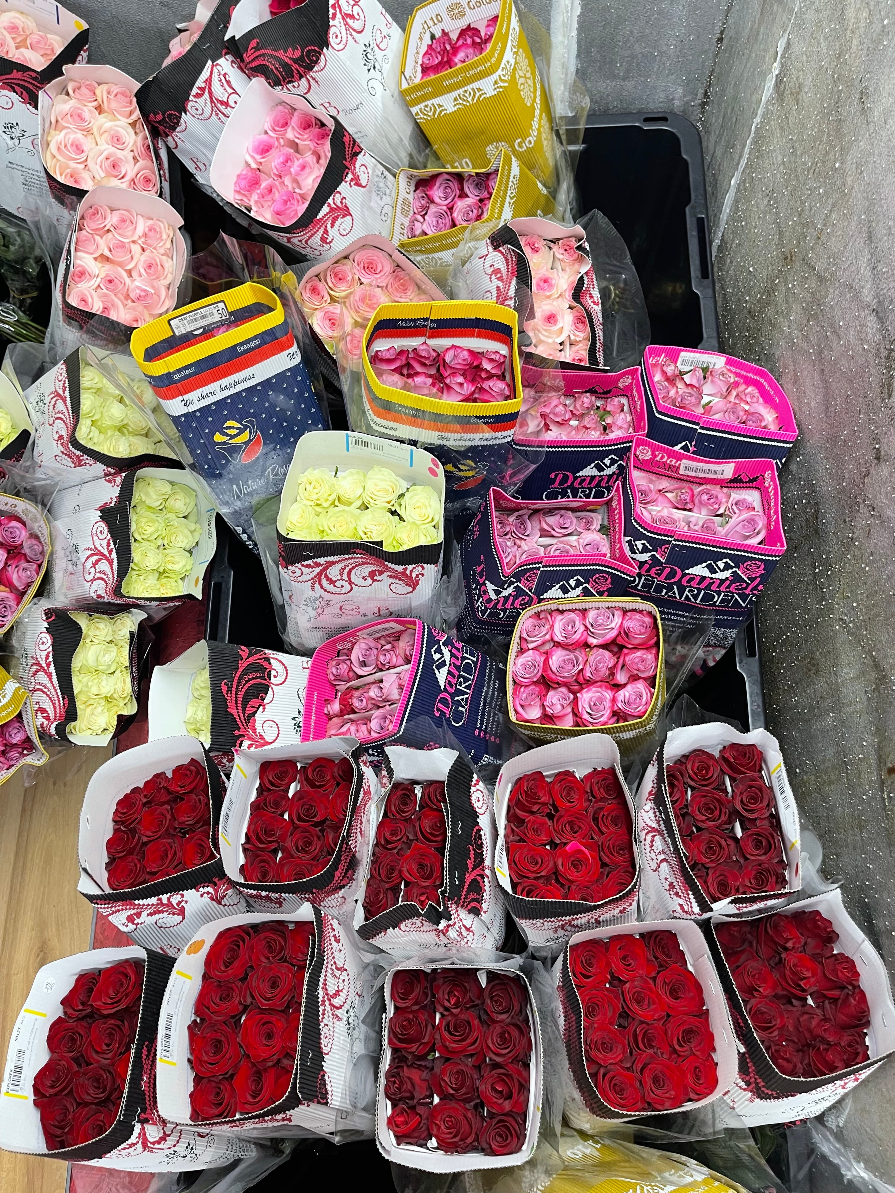 Numerous bouquets of red, pink, and yellow roses in decorative patterned wraps, seen from above.