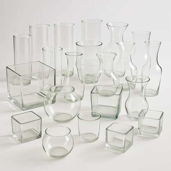 Assorted clear glass vases including cylinders, cubes, and round bowls arranged on a white surface.
